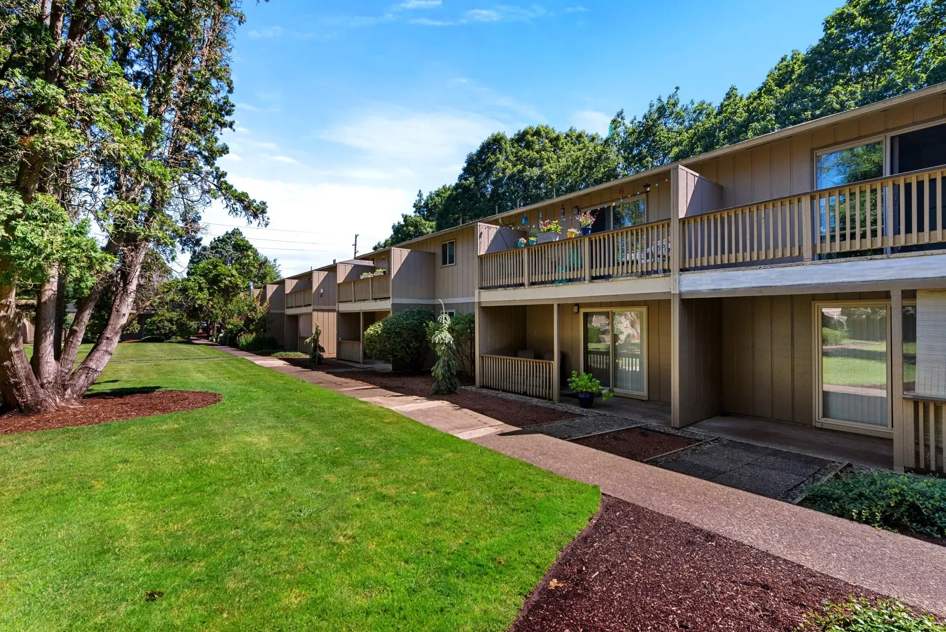 Apartment complex courtyard with green lawn, trees, and two-story balconies under a clear sky
