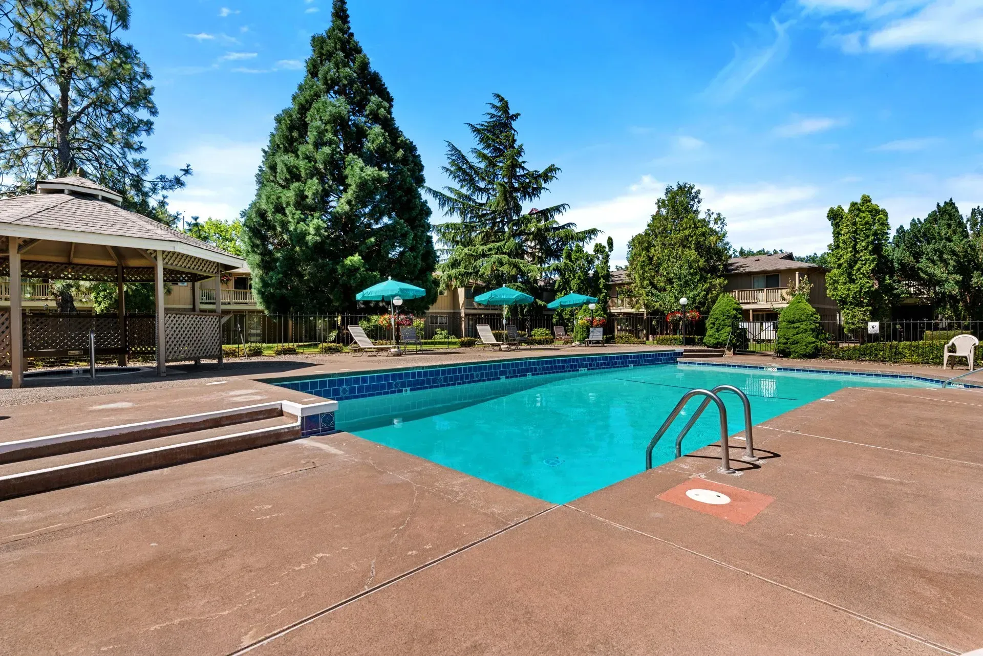 Outdoor swimming pool with blue water, lounge chairs, and umbrellas surrounded by trees and patio decking