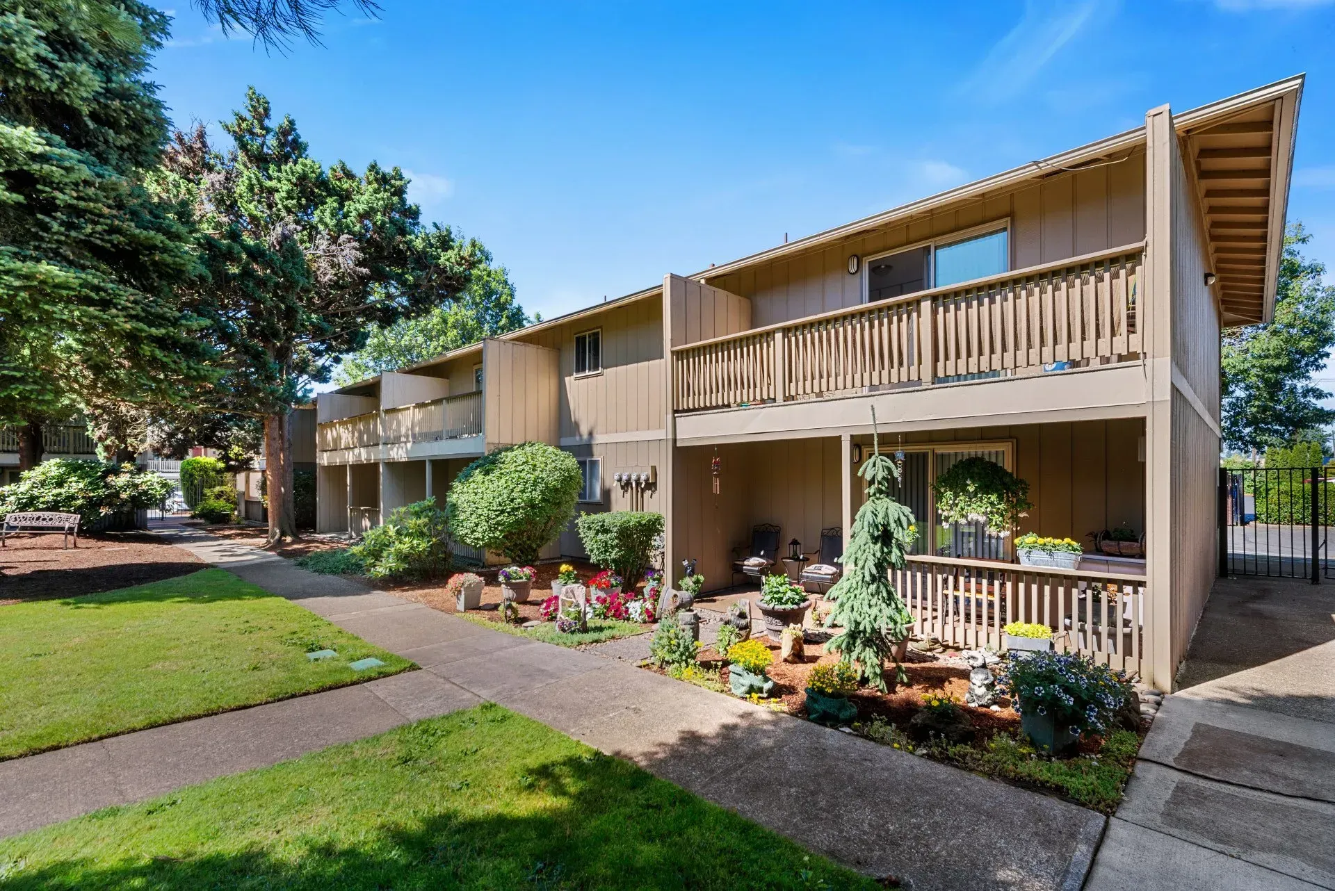 Two-story apartment building with balconies, landscaped walkway, and green lawn under a blue sky