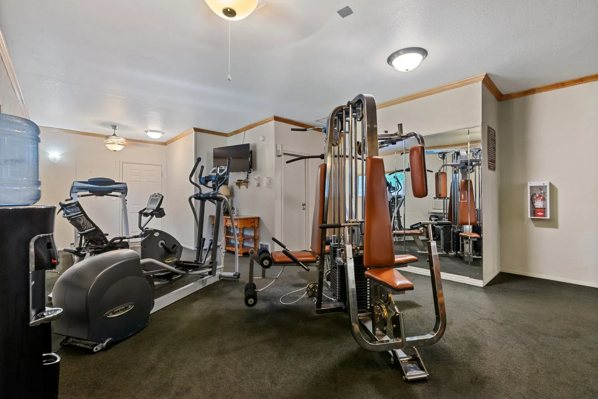 Small gym room with exercise machines, mirrors, and carpeted floor