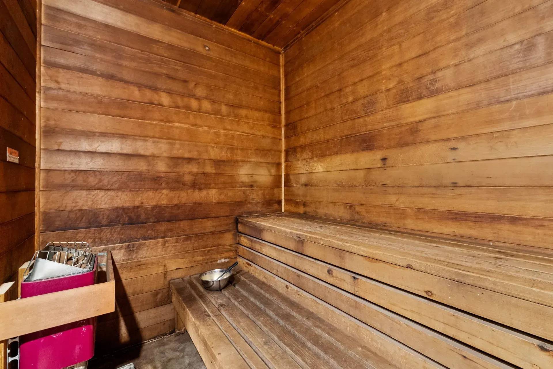 Wood-paneled sauna with wooden benches and a metal bowl on the floor