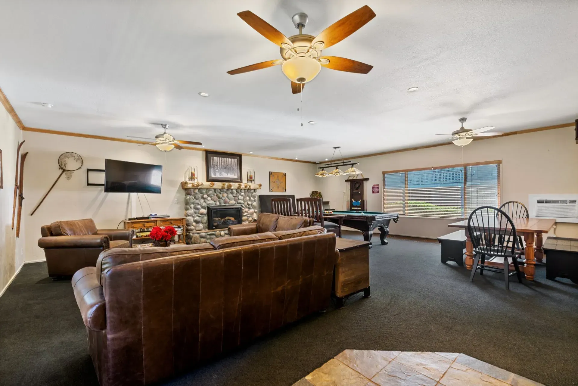 Spacious living room with brown sofa, stone fireplace, ceiling fan, TV, piano, and dining table.