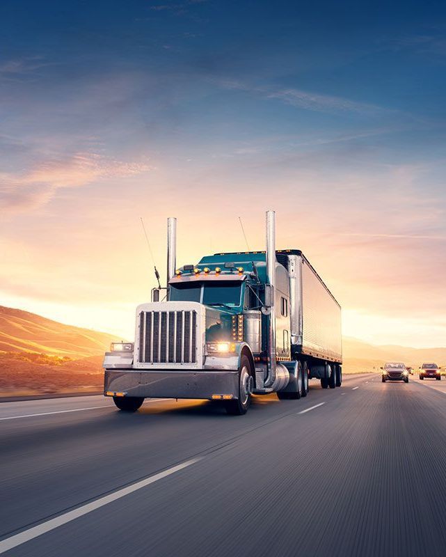 A semi truck is driving down a highway at sunset.
