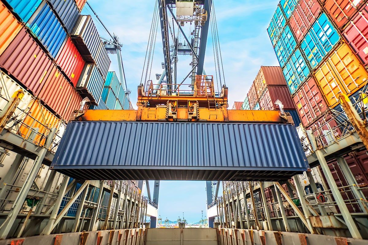 A large container is being lifted into a ship in a harbor.