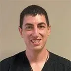 Smiling man with short dark hair wearing a black shirt against a neutral wall.