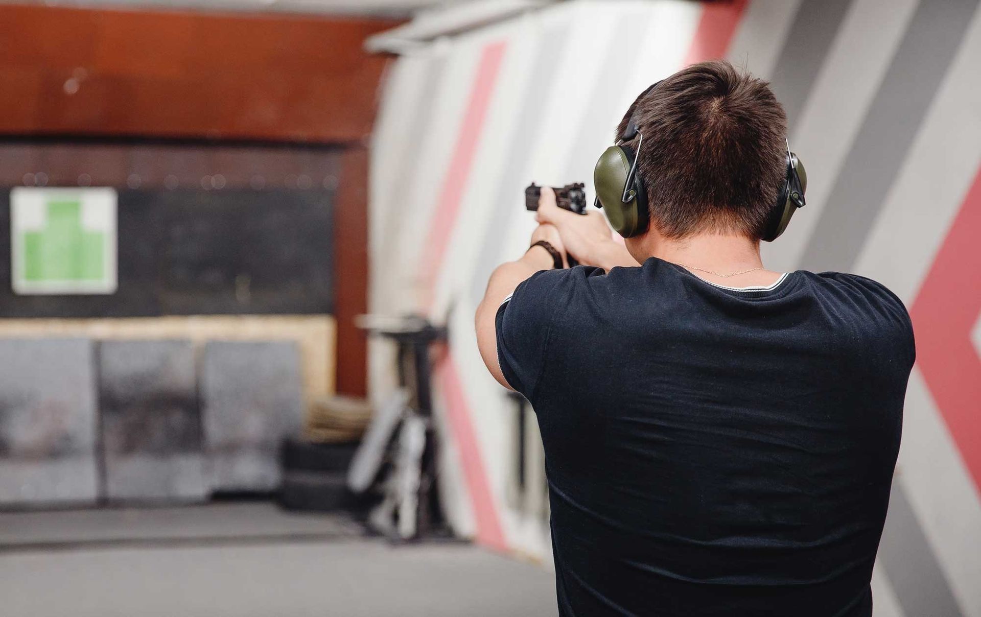 Person aiming a handgun at a shooting range, wearing ear protection and a black shirt