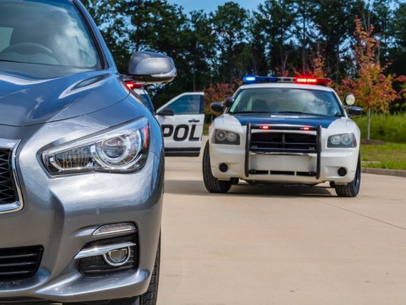 Police car behind silver sedan on a road, with flashing lights and a partial police vehicle in the background
