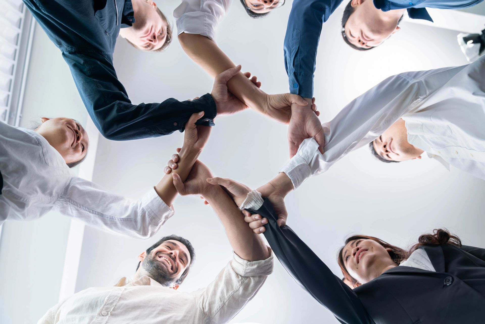 Colleagues in a circle, stacking hands together in a team huddle against a bright background
