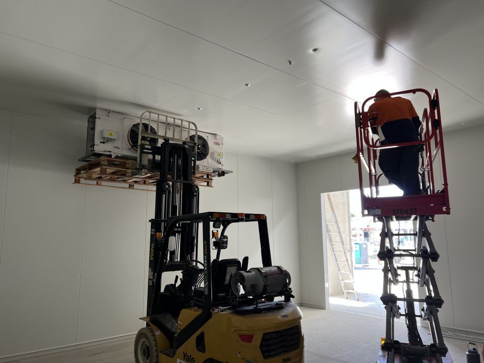 A Man is Standing on a Ladder Next to a Forklift in a Room — Chillzone Refrigeration and Air Conditioning in Beerwah, QLD
