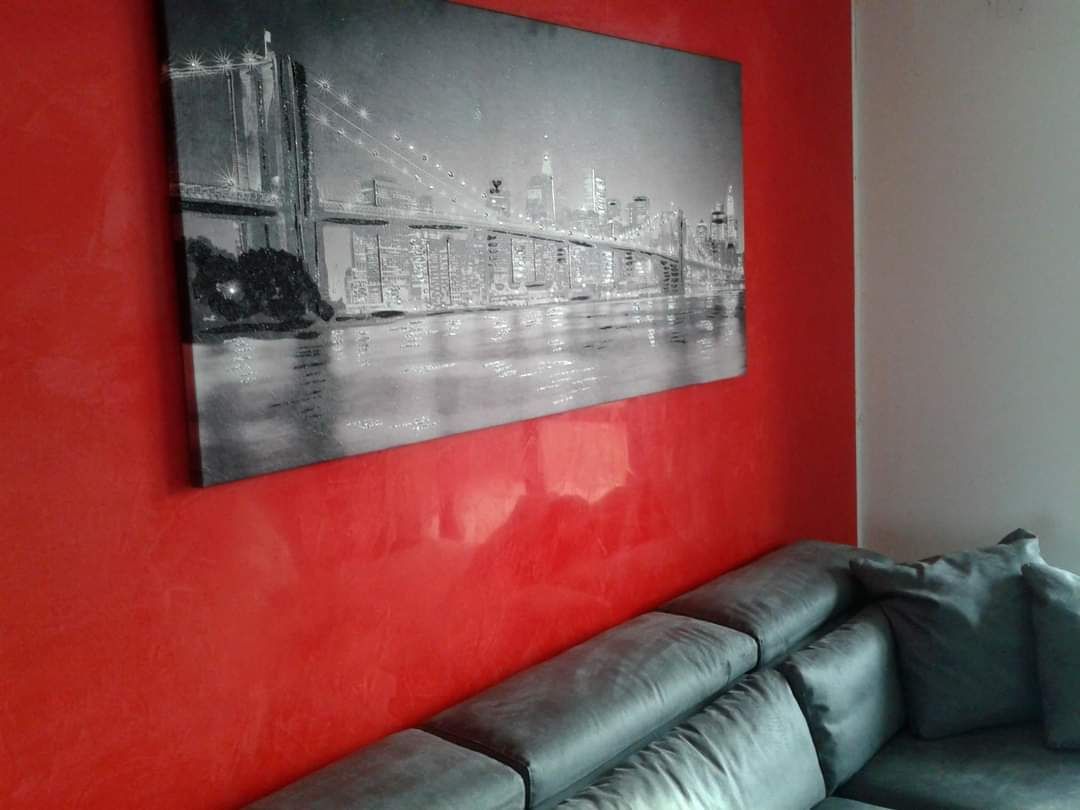 Quadro urbano in bianco e nero su una parete rossa, con un divano grigio di fronte.