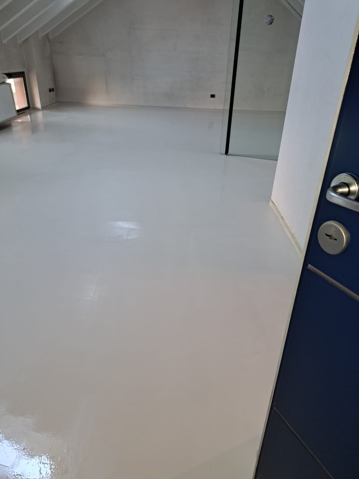 Pavimento in resina epossidica grigio chiaro in una stanza con pareti bianche e una porta blu.