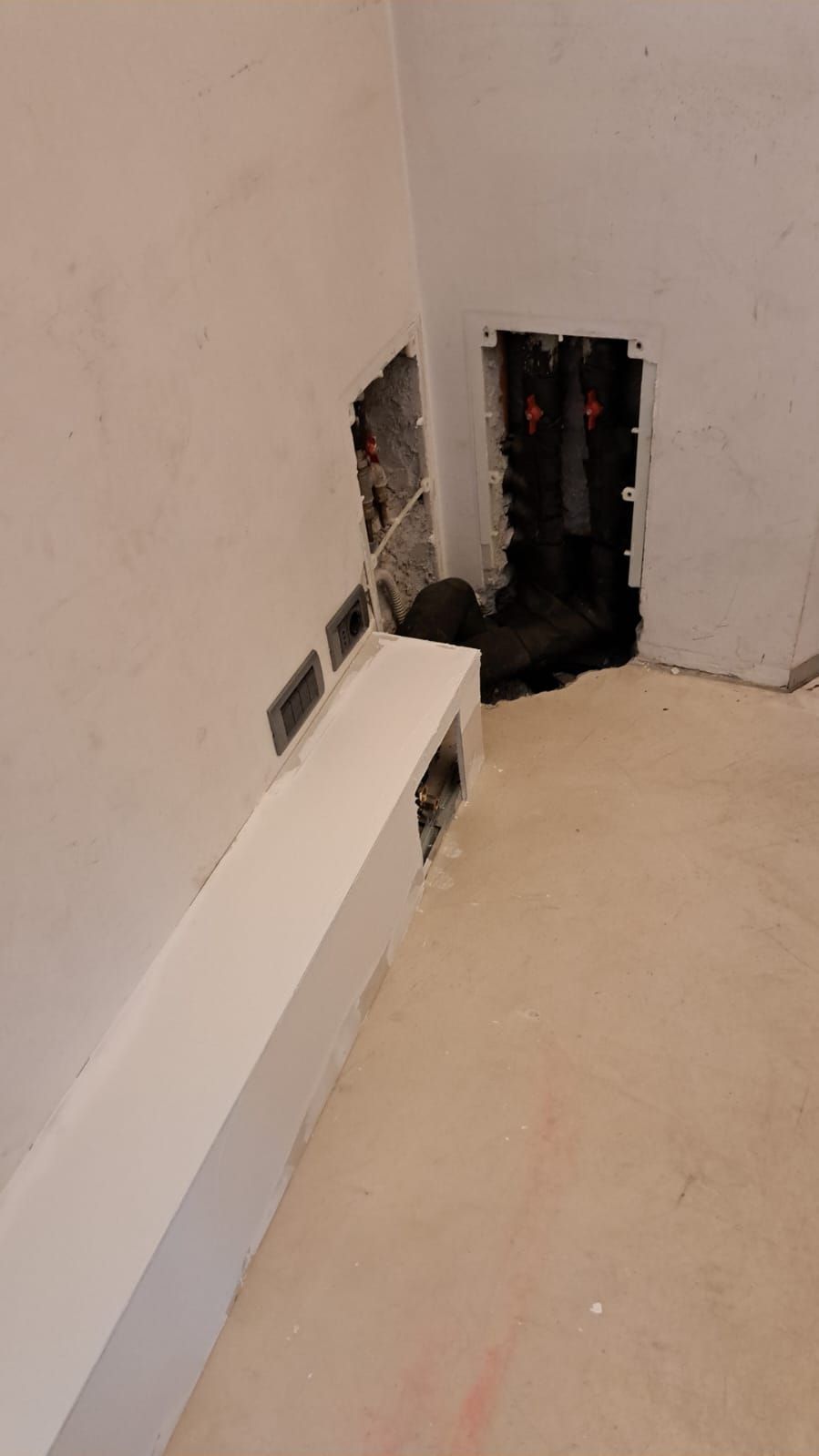 Angolo interno con parete grezza con scatole elettriche e cavi a vista. Battiscopa bianco.