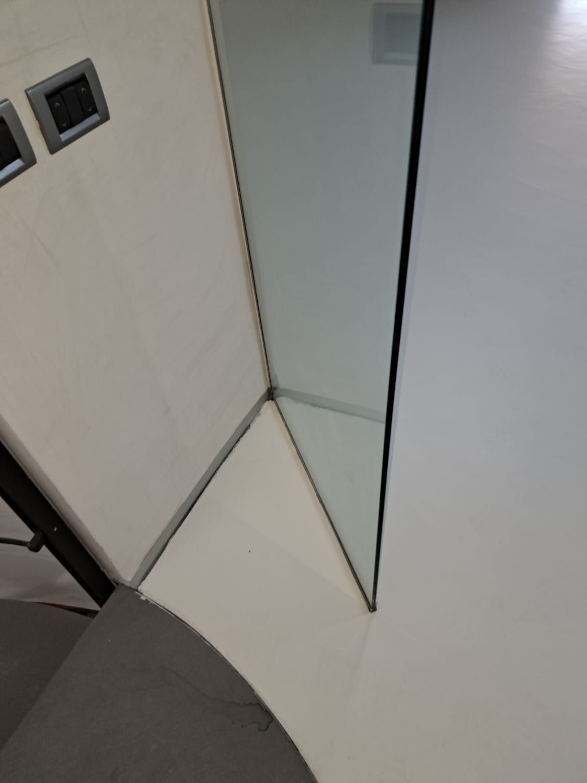 Angolo di una cabina doccia con pannelli in vetro trasparente e pareti bianche.