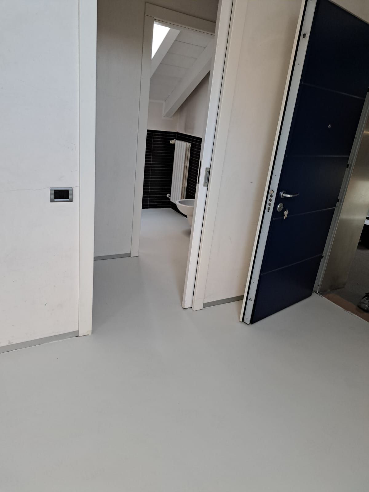 Corridoio grigio con porte bianche e blu, soffitto spiovente.