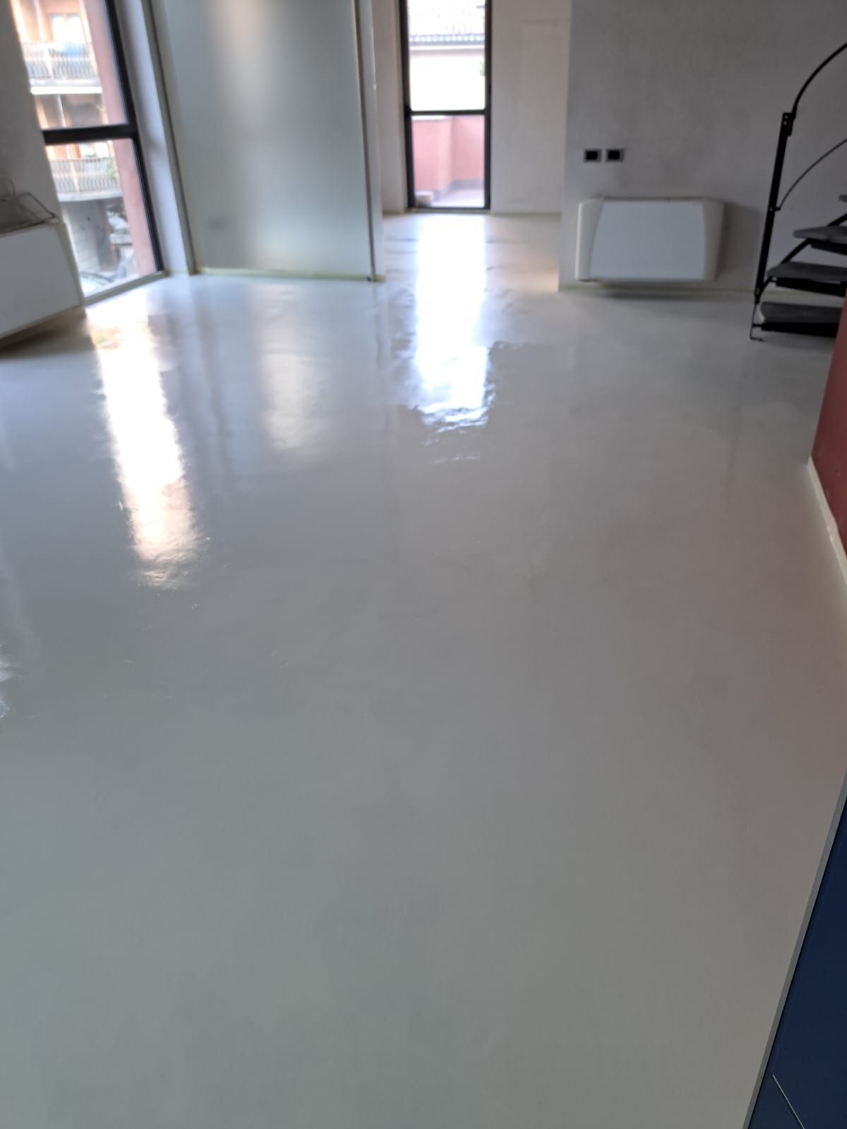 Pavimento bianco lucido in una stanza, che riflette la luce. Finestre, porta e termosifone sullo sfondo.