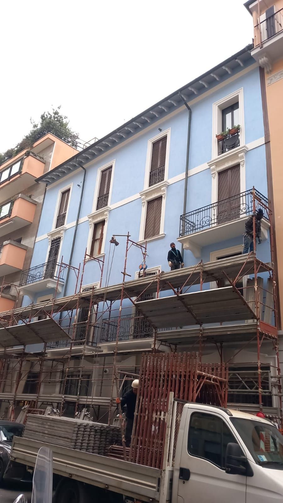 Lavori in corso su un edificio azzurro con impalcature. Si vedono gli operai.