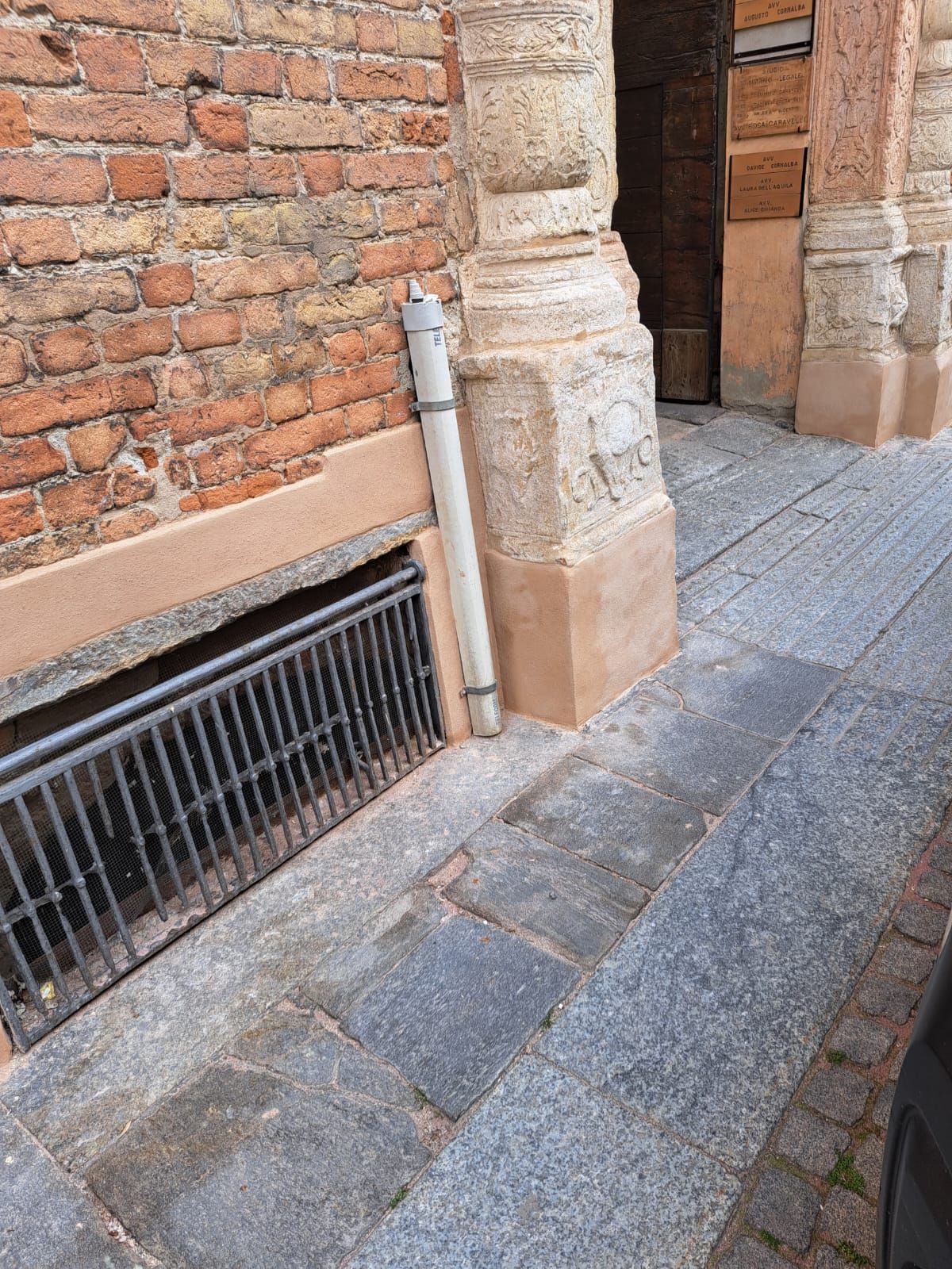 Facciata di un edificio in mattoni con una finestra nel seminterrato con grata e gradini in pietra su una strada acciottolata.