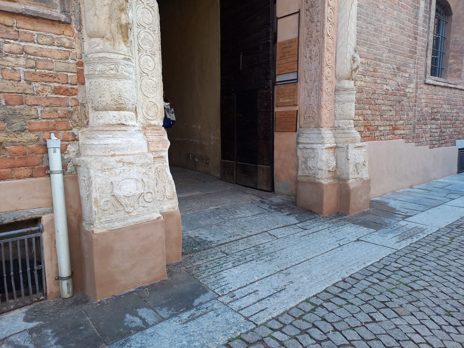 Ingresso di un edificio in mattoni con pilastri, una porta di legno scuro e un sentiero acciottolato.
