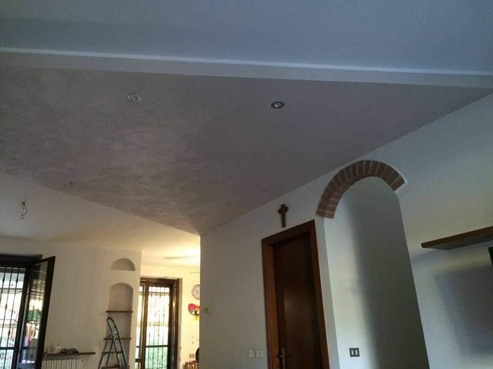 Vista interna di una stanza con soffitto strutturato, porta ad arco e porta di legno.