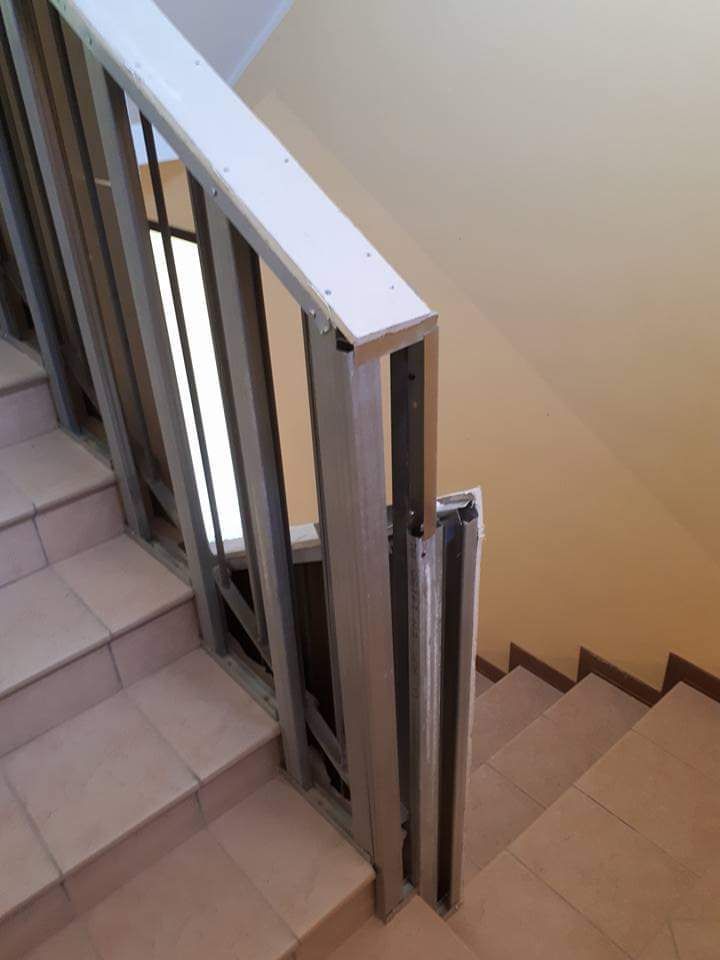Scala con ringhiera in metallo in un edificio, scale e parete color marrone chiaro, corrimano bianco.