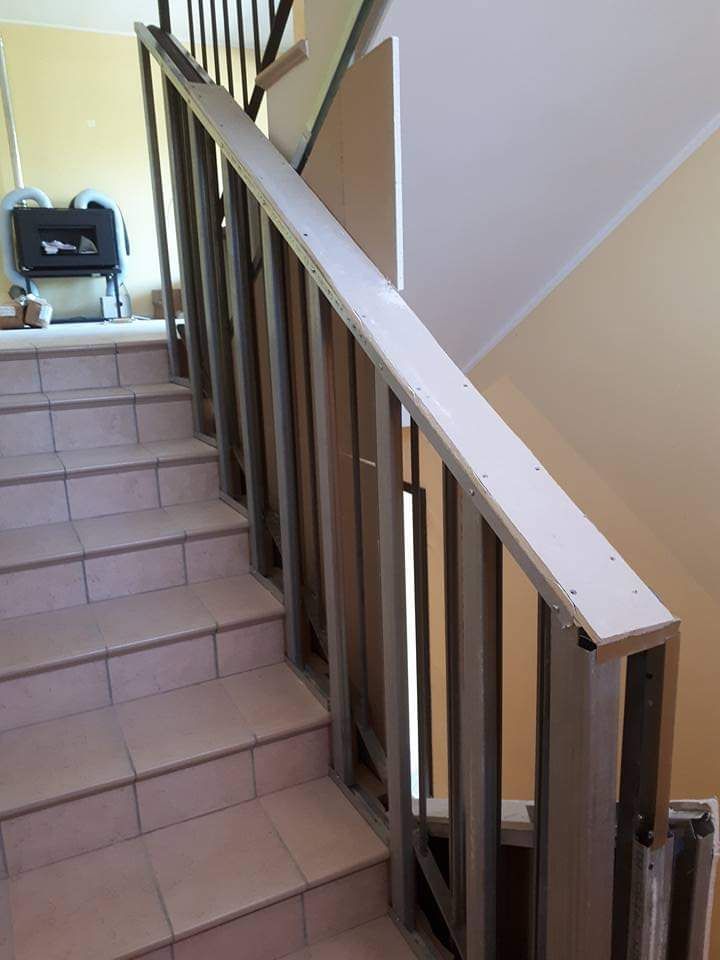 Scala con gradini in piastrelle chiare, ringhiera in metallo e corrimano in legno bianco.