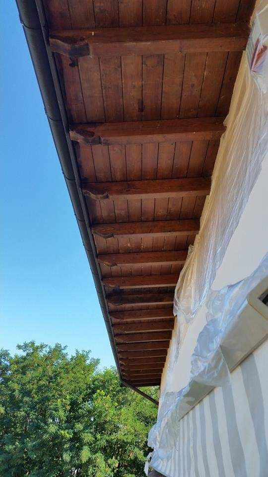 Grondaia in legno di un edificio con grondaia, sostenuta da staffe, contro un cielo azzurro.