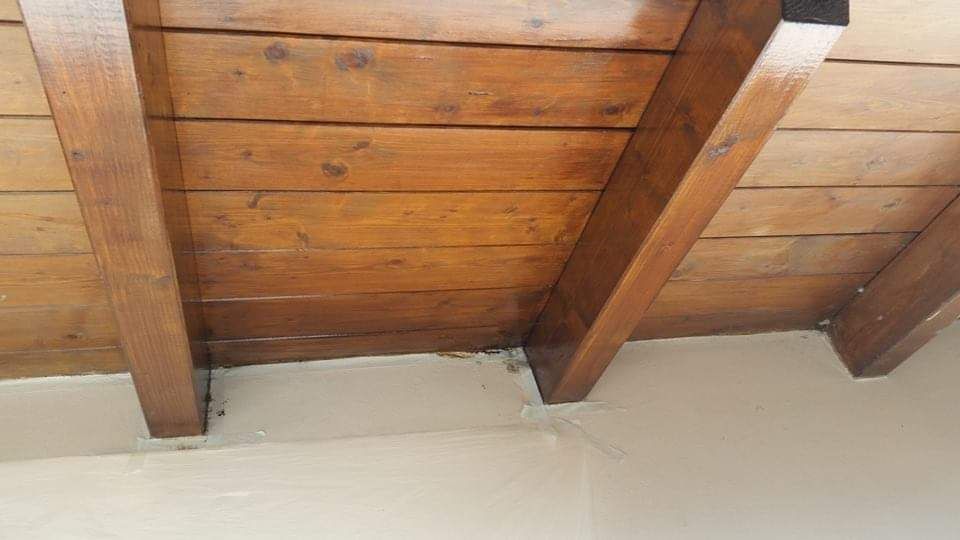 Soffitto in legno con travi di sostegno contro una parete di colore chiaro.