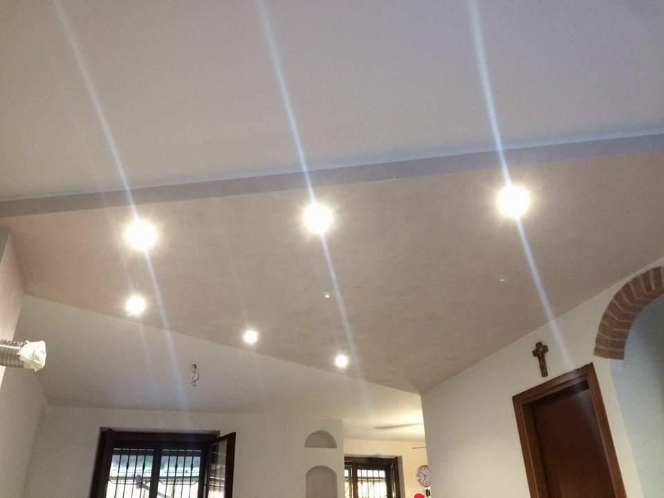 Soffitto bianco con luci incassate; porta ad arco, porta marrone, finestra visibile.