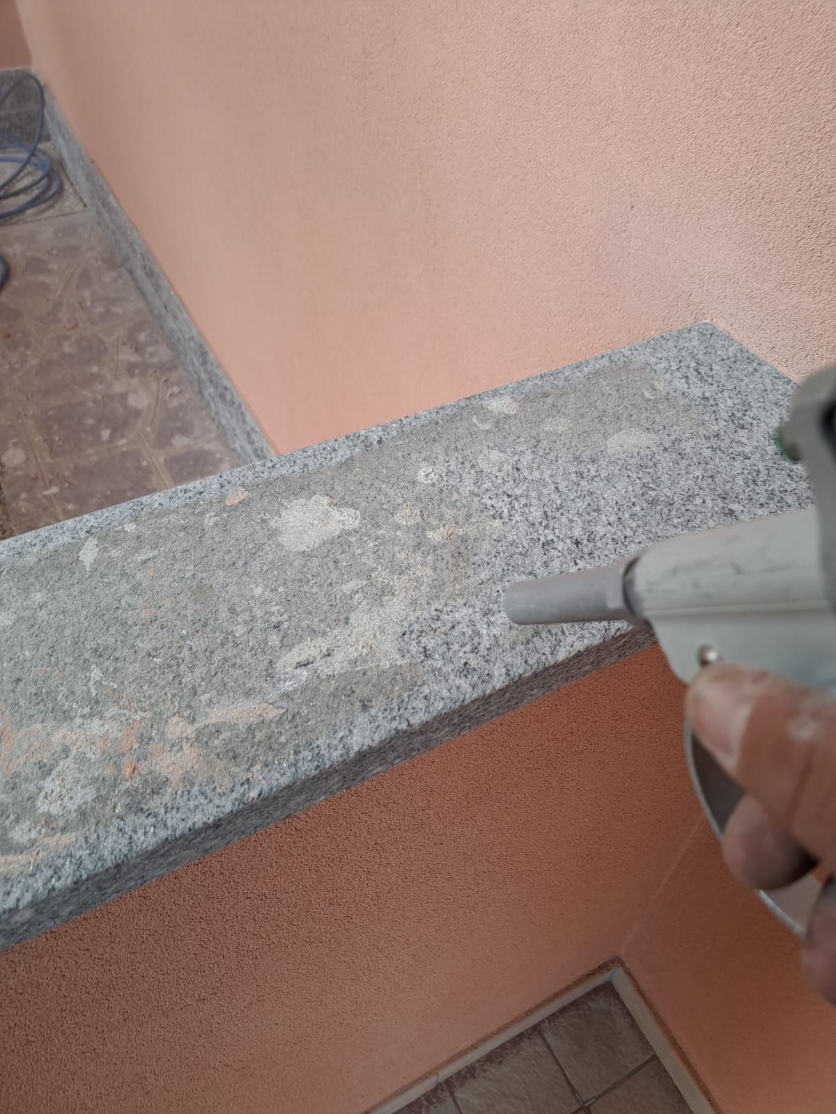 Una persona spruzza cemento con un attrezzo, sullo sfondo un muro arancione.