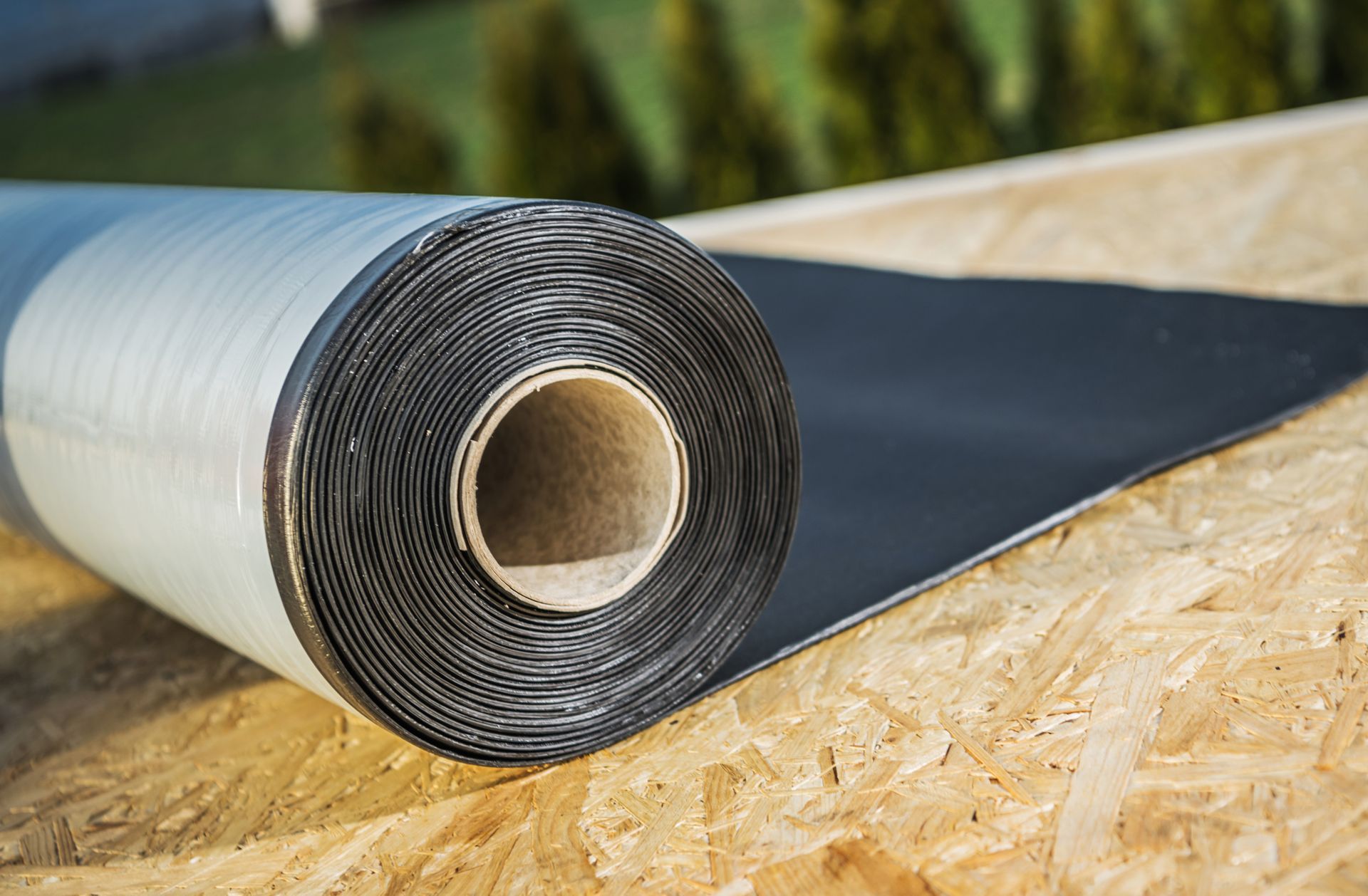 Roll of black roofing material on an unfinished wooden surface.