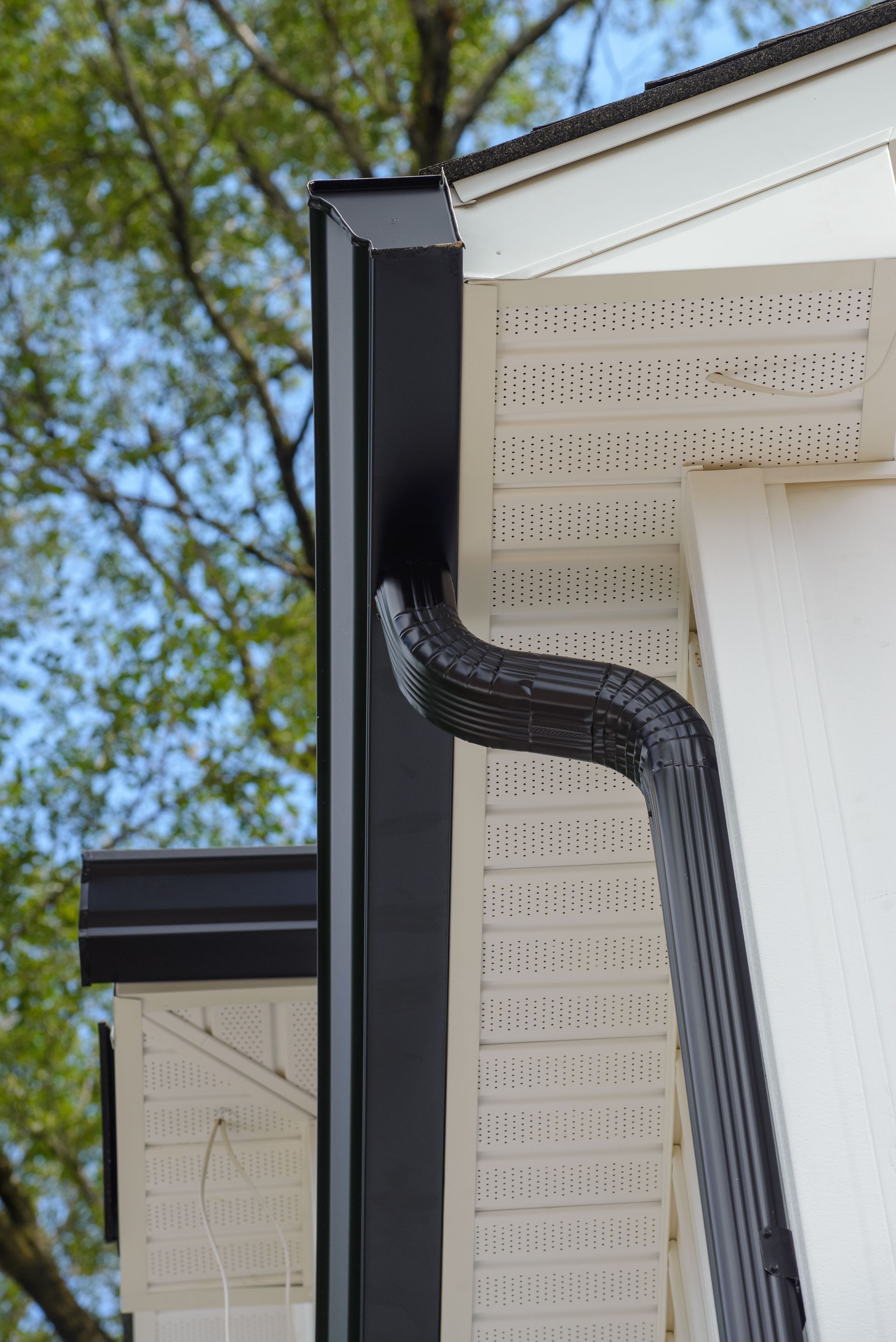 Black gutter and downspout on a white house exterior.