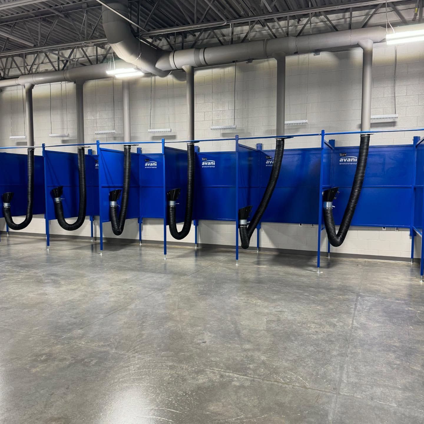 Blue industrial dust collection booths with black hoses in a warehouse shop area