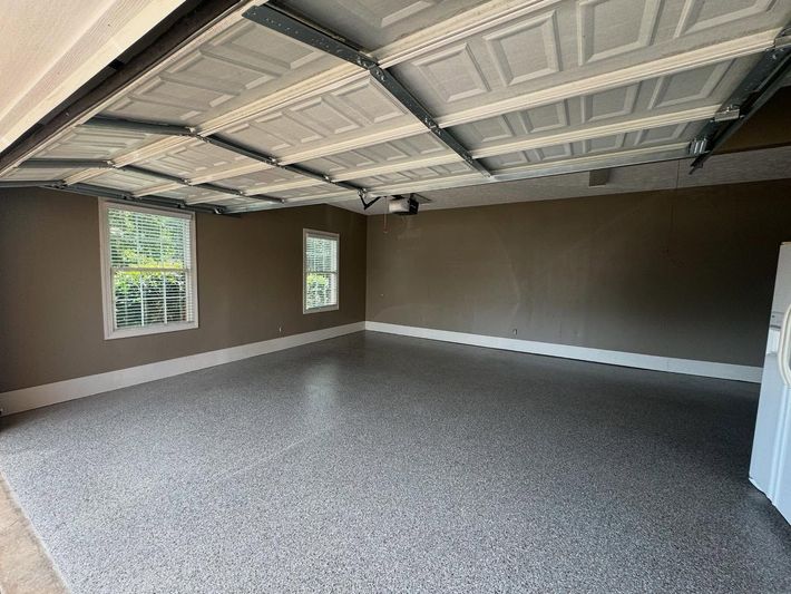 Empty garage interior with gray speckled floor, dark walls, and open paneled ceiling.