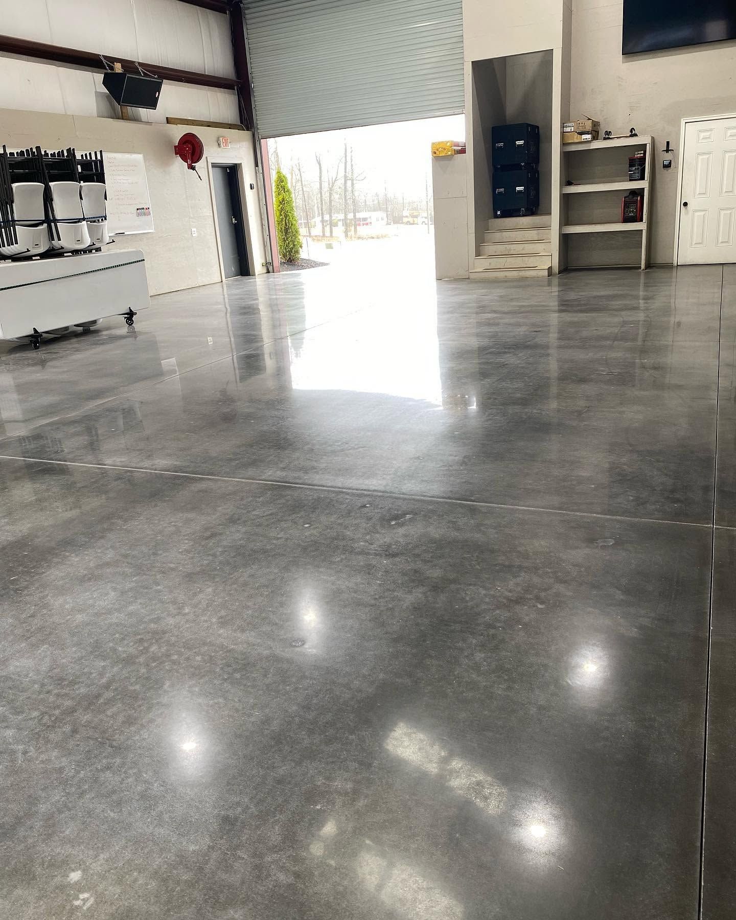 Empty industrial warehouse with polished concrete floor and bright open doorway in the back.