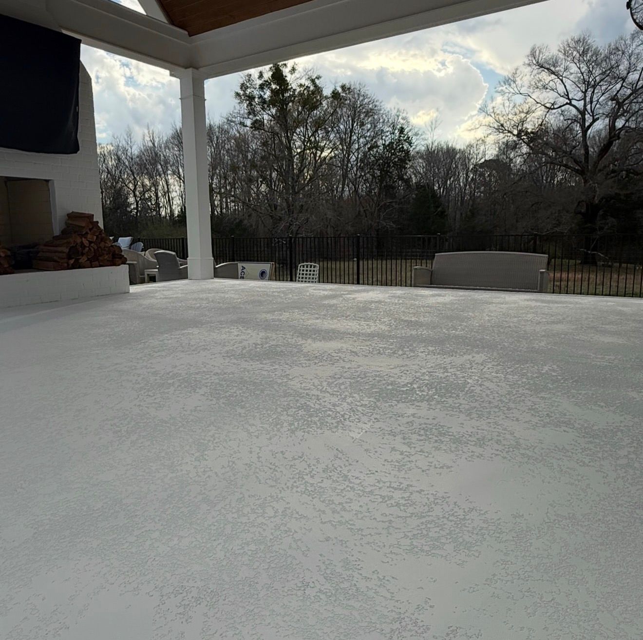 Snow-covered patio under a roof, with trees and a cloudy sky in the background.