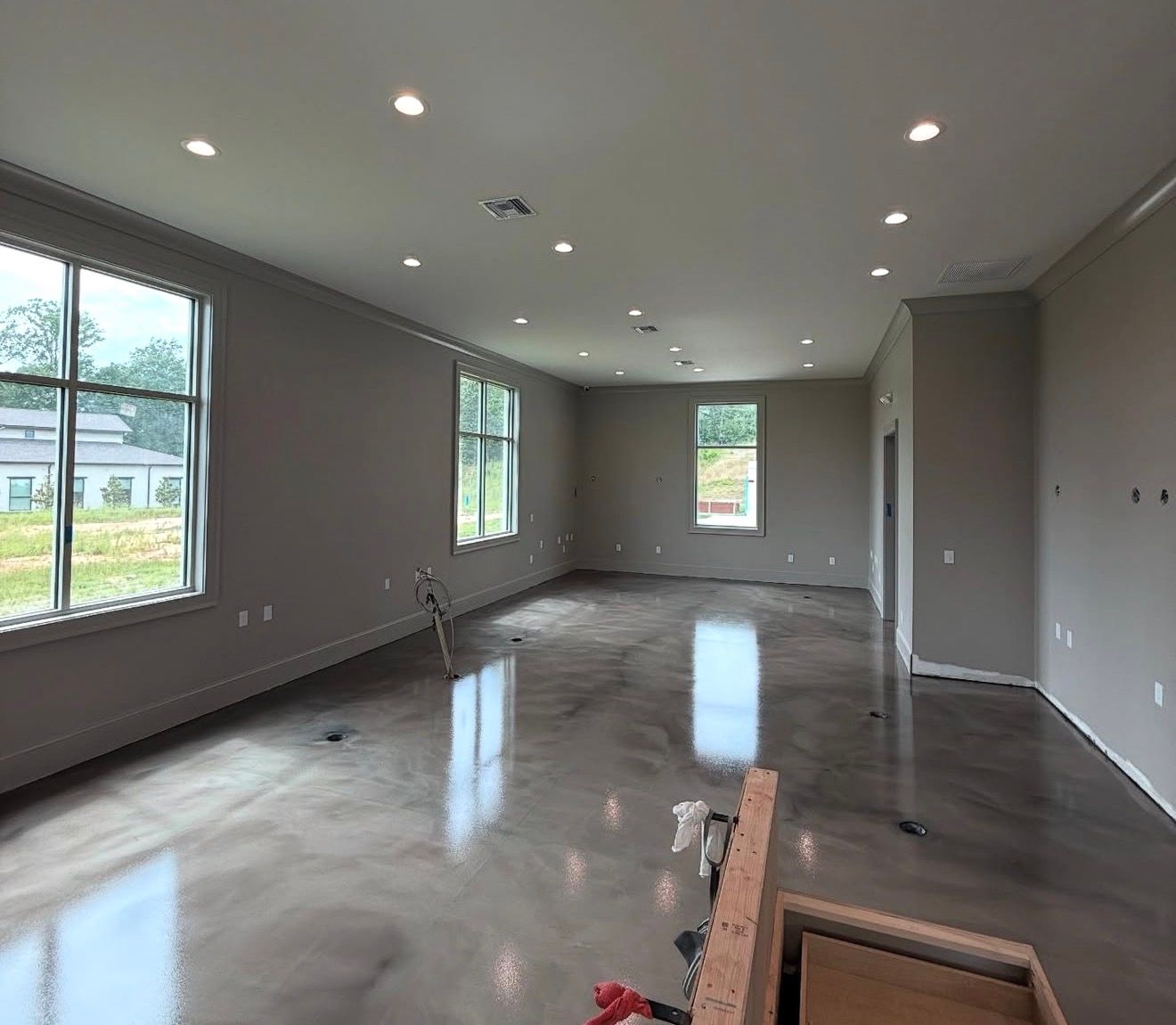 Empty modern living room with gray walls, polished floors, recessed lights, and large windows.