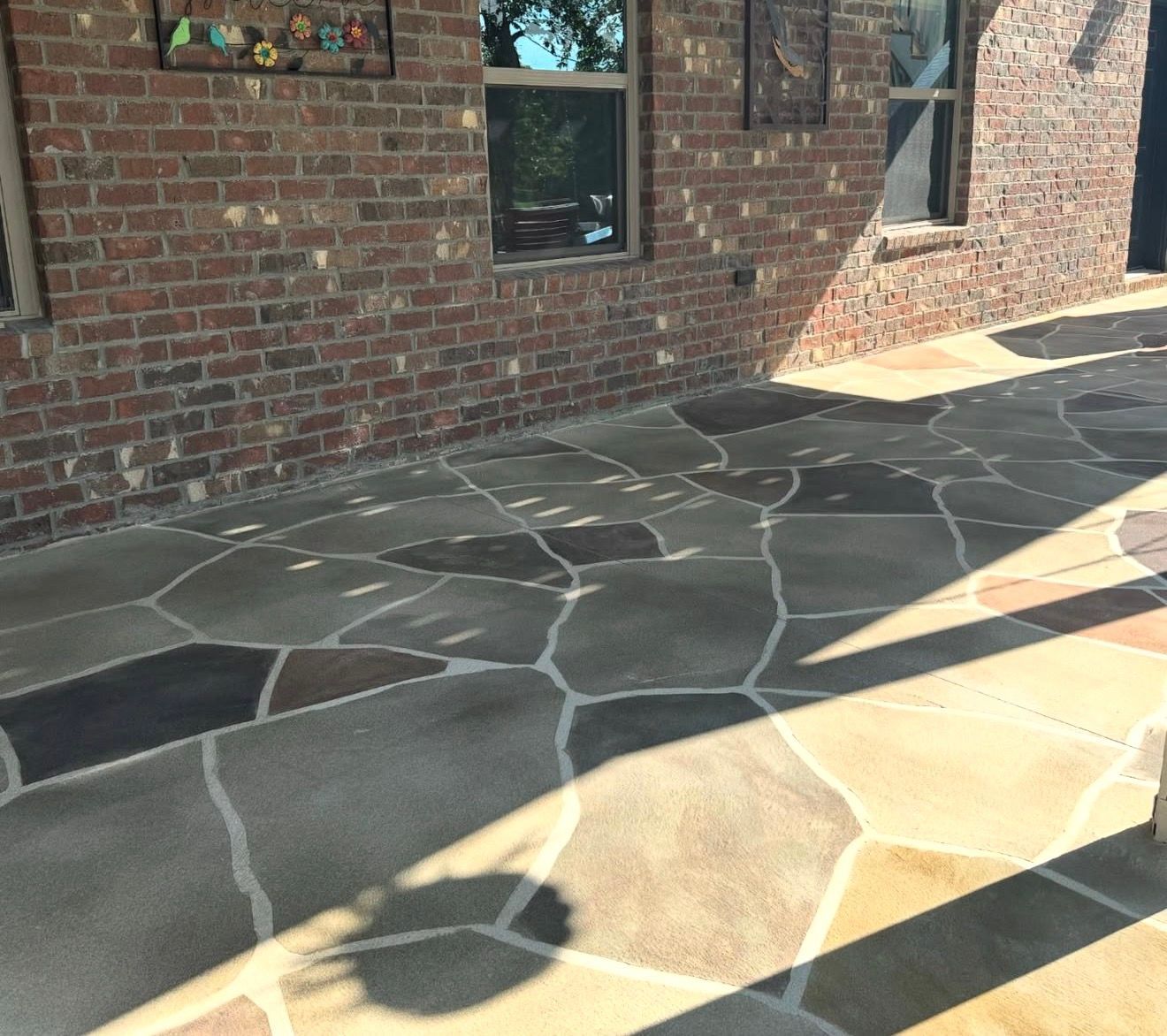 Brick house wall with windows and a stone patio in sunlight and shadow
