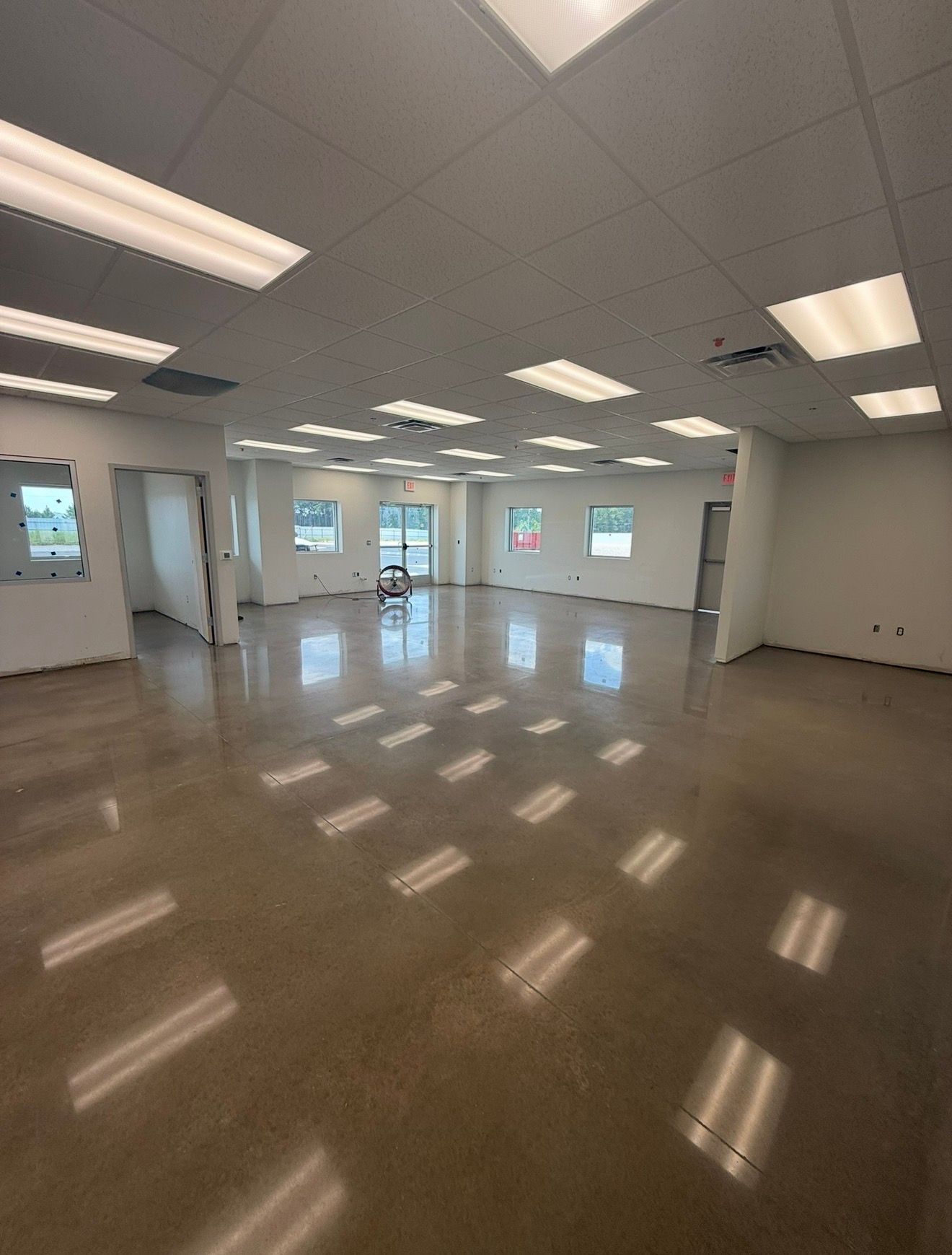 Empty, bright office space with tiled ceiling, glossy floor, and large windows.