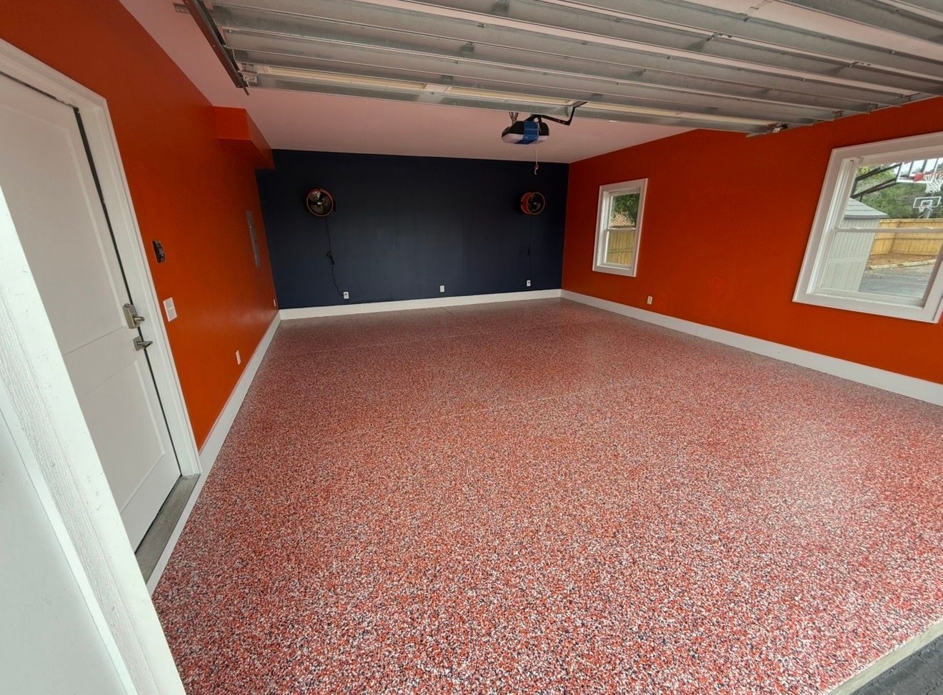 Empty room with orange walls, dark accent wall, white ceiling, and speckled red floor.