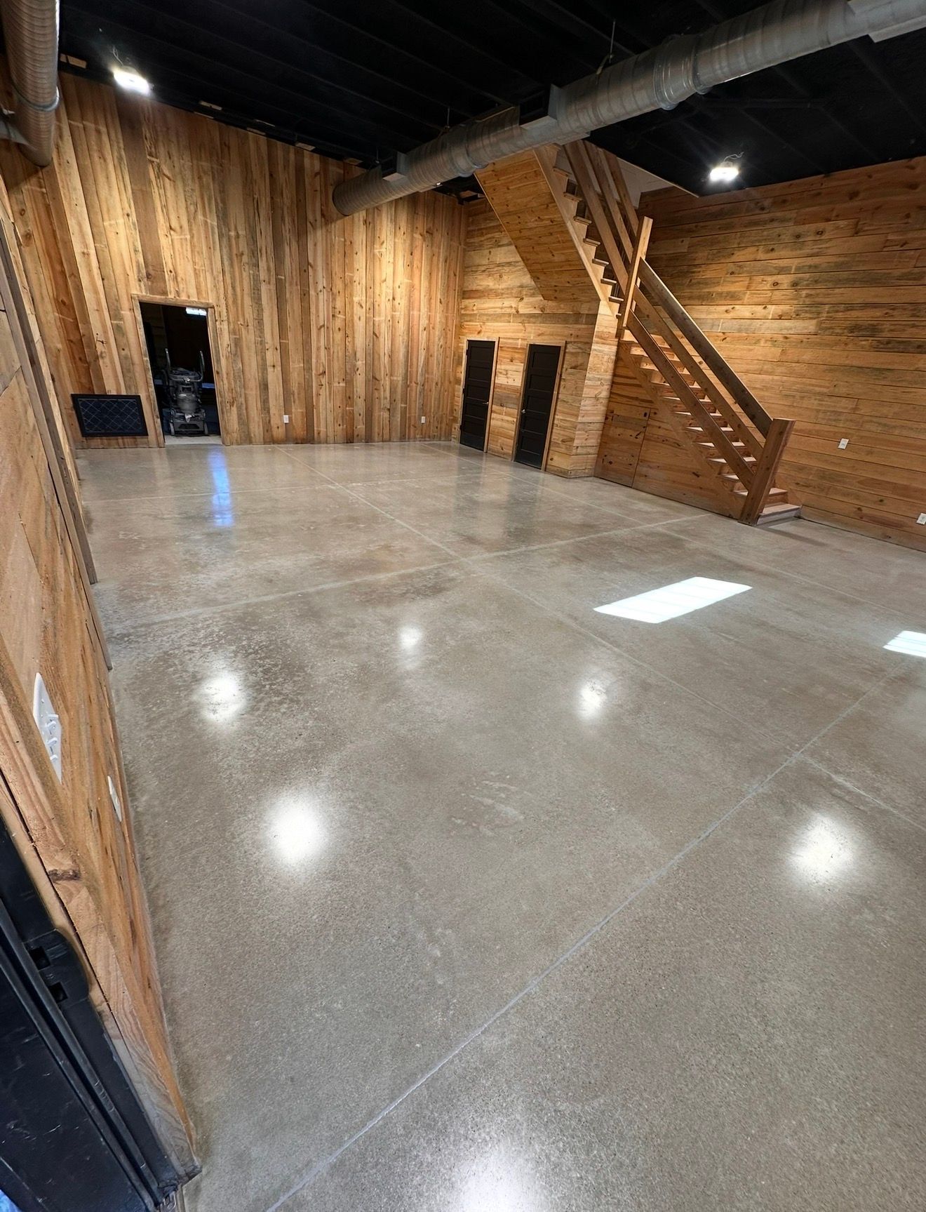 Empty polished concrete room with wood-paneled walls and a staircase on the right.