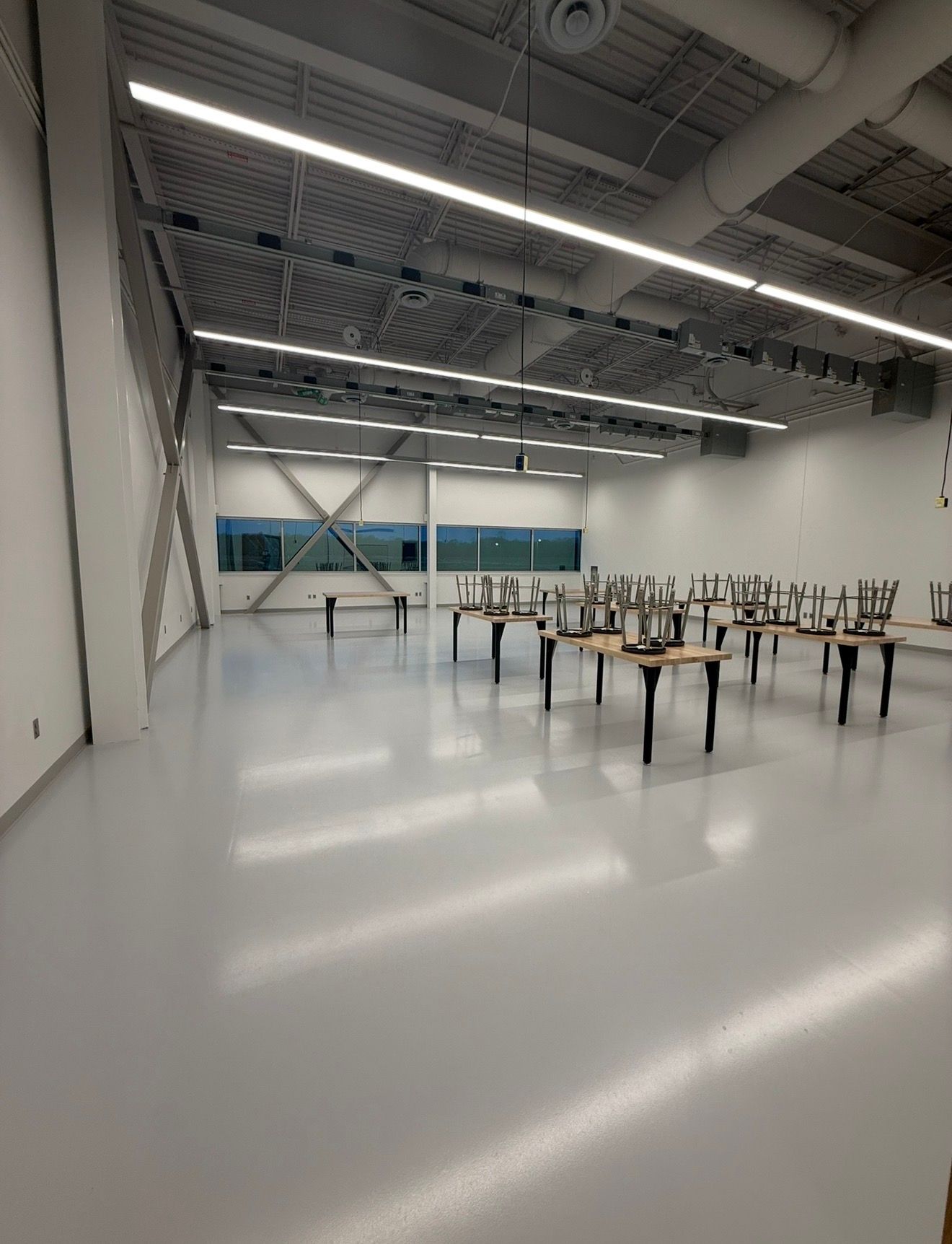 Large empty warehouse-like room with tables, chairs stacked upside down, and bright overhead lights