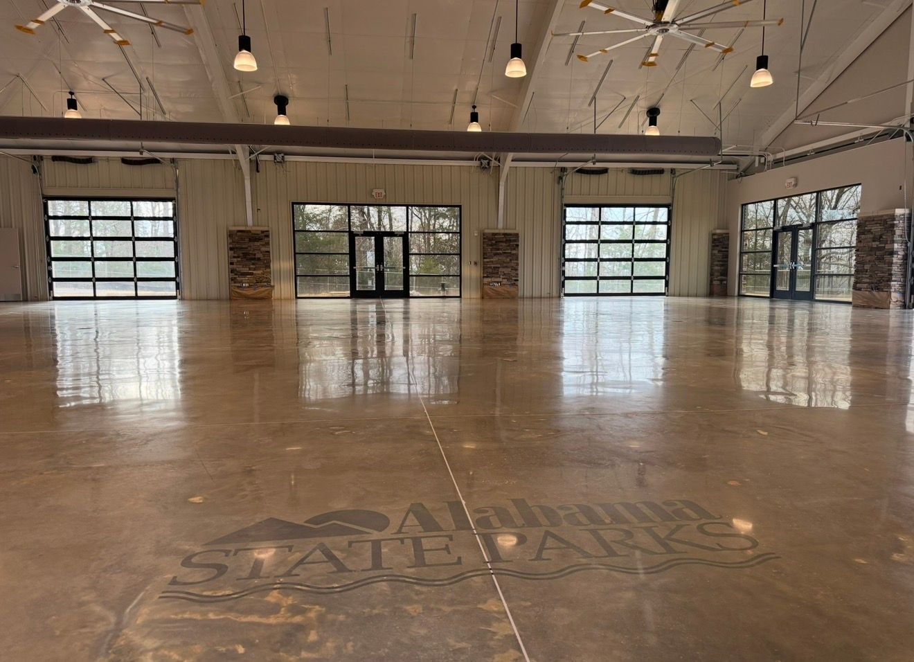 Spacious empty hall with polished concrete floor, hanging lights, and large garage-style windows.