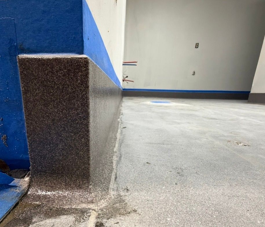 Indoor concrete floor beside a blue-and-white wall with a raised dark speckled corner post.