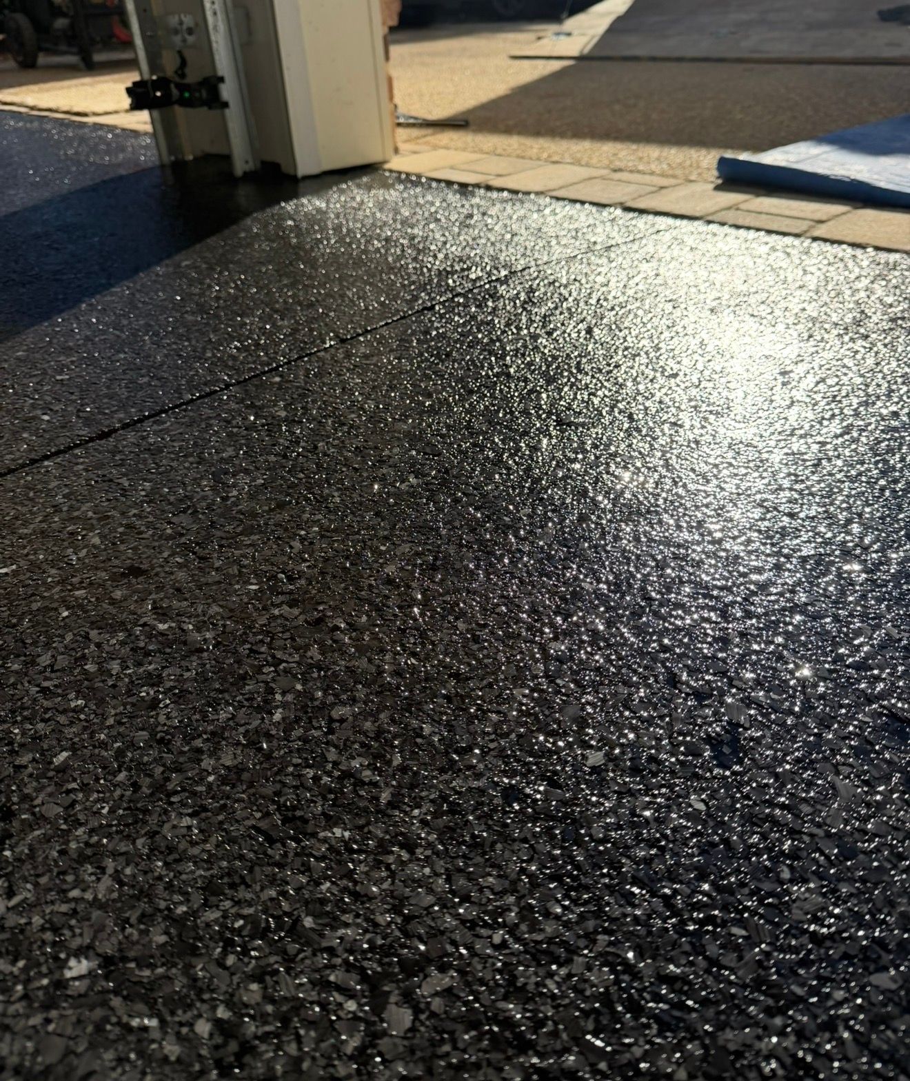 Sunlit black textured floor beside a doorway, with bright light reflecting on the surface.