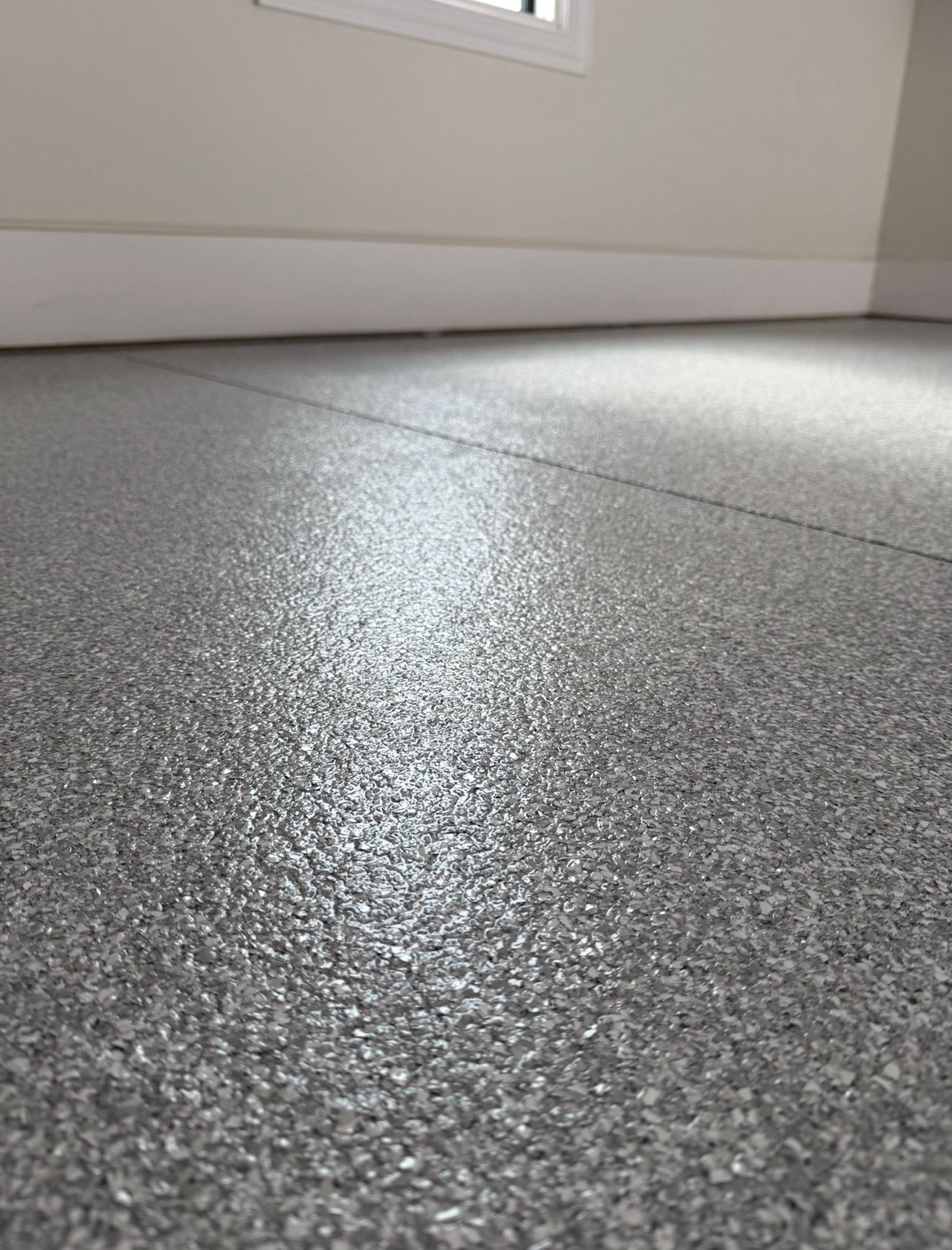 Textured gray floor under a white wall and window in a bright empty room