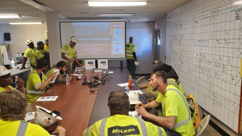 People in neon safety shirts gathered in a conference room for a presentation and discussion.
