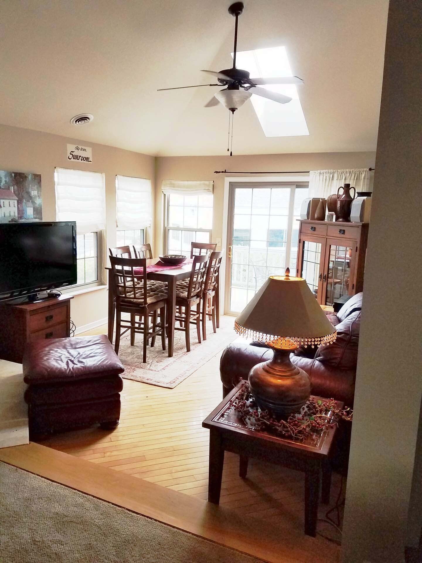 Cozy living room with dining area. Brown furniture, overhead fan, sunlight through skylight and sliding doors.