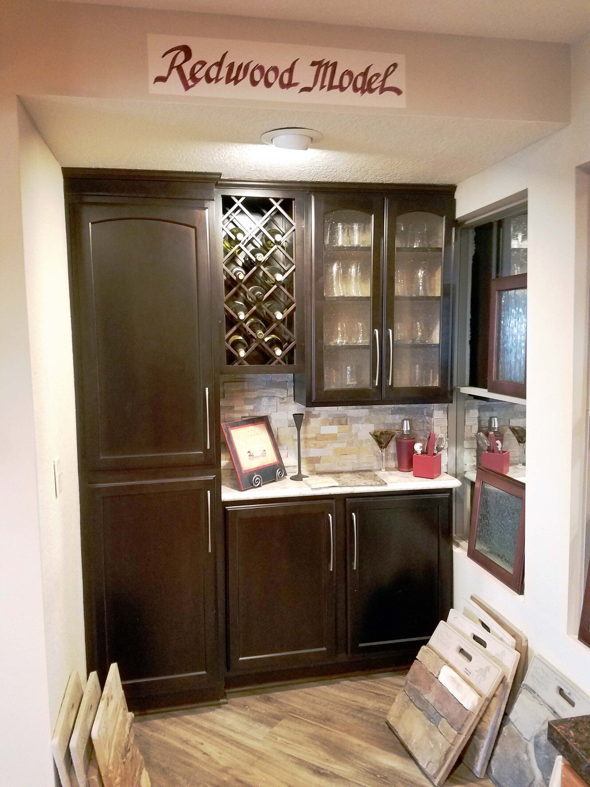 Dark wood bar cabinet with wine rack and glass-front cabinets in a showroom setting.