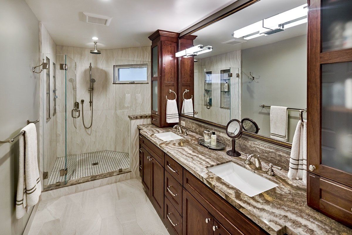 Bathroom with dark wood cabinets, marble countertop, glass shower, and large mirror.