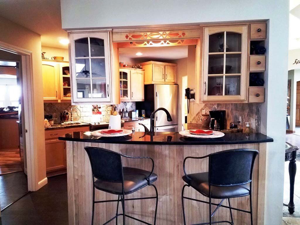 Kitchen with a breakfast bar, two stools, cabinets, and view of the kitchen with black countertops.